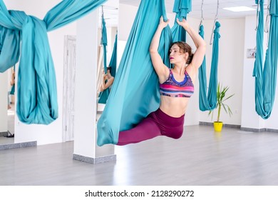 woman 25 years old is hanging using blue hammock for yoga. Lady wearing in light blue sportswear