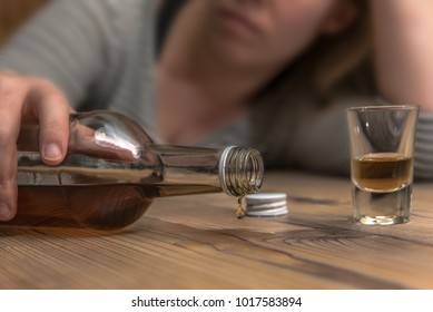 A Woman (25-30) Spills Alcohol From An Upturned Bottle Of Brandy At The Table. Concept: Alcohol Abuse Or Drinking