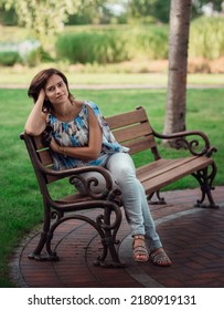 Woman 40 Years Old Sits On A Bench In The Park. Summer, Trees, Silence.
Woman In Jeans And Blouse. Average Age