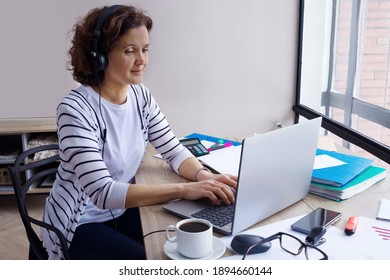 A woman of 40-45 in a headphones works at a laptop at home. - Shutterstock ID 1894660144
