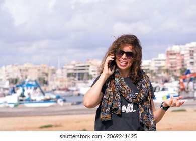 Woman 45+ Years Old Talking On A Smartphone Against The Background Of A Seaside City In Sunny Weather