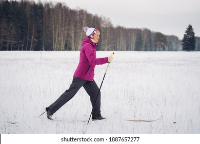 A Woman Of 50 Years Old Goes Skiing In The Snow On The Background Of The Forest