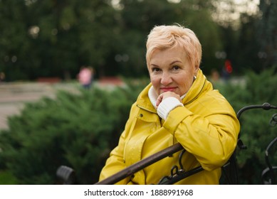 Woman Of 50s Walking In The Park And Wearing Bright Yellow Raincoat. Active Lifestyle. Young Grandmother Walking With Stroller. 