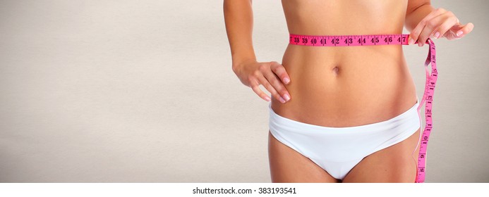 Woman abdomen with measuring tape over grey background.