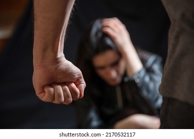 Woman abuse, Young woman scared holding head with hands, male clenched fist close up. Domestic violence, husband against wife. Dark room background

