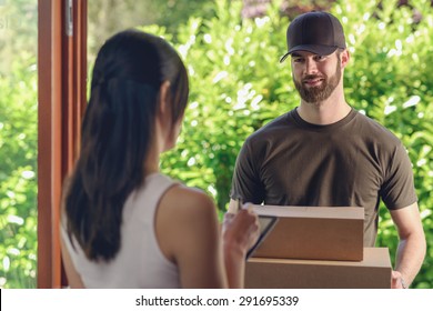 Woman accepting a delivery of two cardboard boxes with an order or gift signing the digital clipboard for the friendly smiling deliveryman on the doorstep