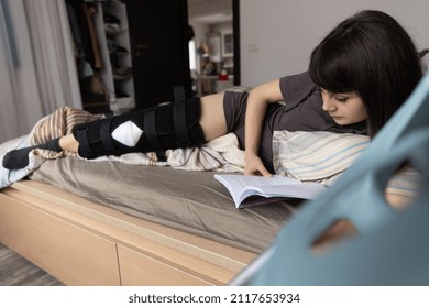 Woman With ACL Surgery Reading In Bed At Home With Crutches Nearby.