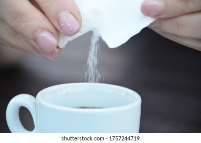 Woman With Acrylic Finger Nails Pouring Sugar From A White Sugar Packet In A Cup Of Coffee