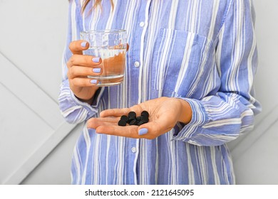 Woman with activated carbon pills and glass of water near wall
