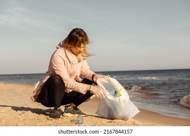 Woman Activist And Assistant Cleaning Sandy Beach From Underwater Trash, Sea Or Ocean With Plastic Waste. Global Change.