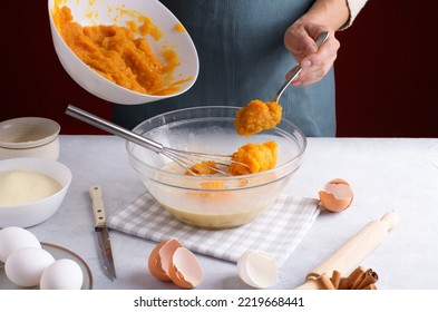 Woman Add A Pumpkin Puree Into A Bowl With Filling For Pumpkin Pie For Mix With Whisk On A Gray Table Surrounded By Ingredients In The Kitchen. Home Cooking Concept, Traditional Pie Recipe