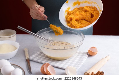 Woman Add A Pumpkin Puree Into A Bowl With Filling For Pumpkin Pie For Mix With Whisk On A Gray Table Surrounded By Ingredients In The Kitchen. Home Cooking Concept, Traditional Pie Recipe