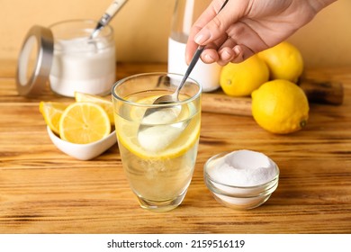 Woman adding baking soda into glass with water on wooden table - Shutterstock ID 2159516119