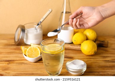 Woman Adding Baking Soda Into Glass With Water On Wooden Table