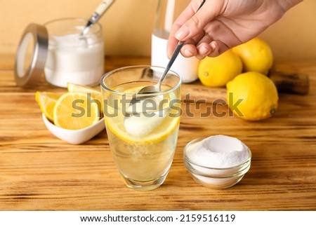 Woman adding baking soda into glass with water on wooden table