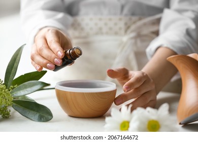 Woman adding essential oil to aroma diffuser on table