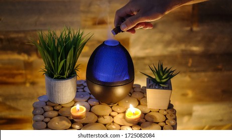 Woman adding essential oil to electric diffuser lamp, candles on wooden table in room. Aromatherapy.