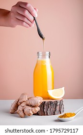 Woman adding honey to immune boosting drink with lemon, ginger, turmeric. Drink or smoothie on wooden stand for autumn or virus season on neutral beige background