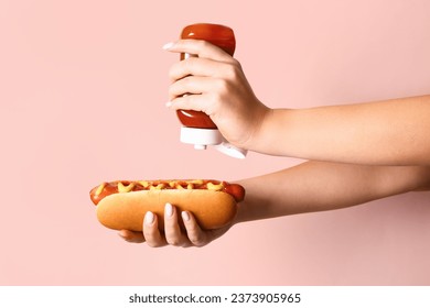 Woman adding ketchup onto tasty hot dog on pink background - Powered by Shutterstock