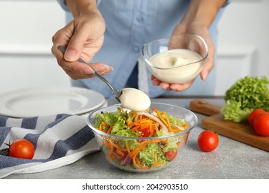 Mujer añadiendo mayonesa a deliciosa ensalada en mesa gris, cerrar