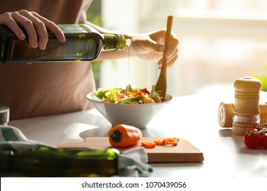 Woman adding olive oil into bowl with fresh vegetable salad on table - Powered by Shutterstock