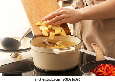 Woman Adding Potato To Cooking Pot In Kitchen