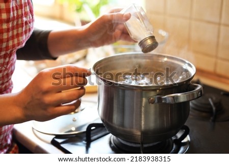 Woman adding salt to boiling water in pot on stove indoors, closeup