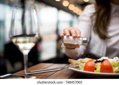 Woman Adding Salt To Food In Restaurant.