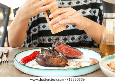 Woman adding salt to steak in restaurant