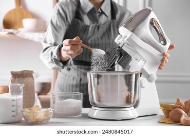 Woman adding sugar into bowl of stand mixer while making dough at table indoors, closeup - Powered by Shutterstock