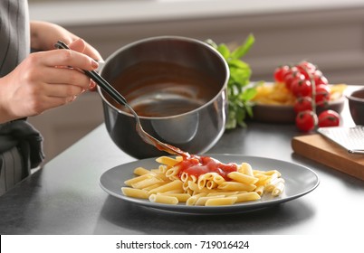 Woman adding tasty tomato sauce to pasta on plate - Powered by Shutterstock