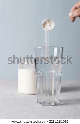 Woman adds collagen powder to a glass of water with a measuring spoon. Healthy and anti-age concept on blue background