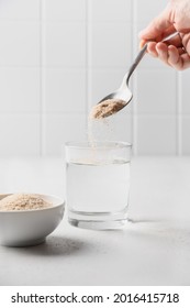 Woman adds psyllium fiber to glass of water on a white background. Superfood for healthy intestines and gluten free diet.