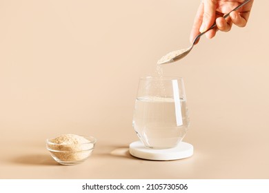Woman Adds Psyllium Fiber To Glass Of Water On Beige Background. Superfood For Healthy Intestines And Gluten Free Diet.