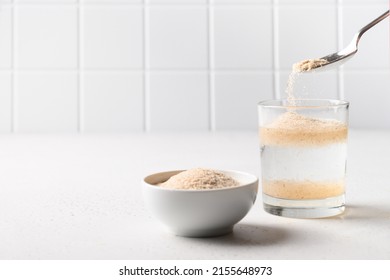 Woman Adds Psyllium Fiber To Glass Of Water On White Background. Superfood For Healthy Intestines And Gluten Free Diet, Boosts Weight Loss.