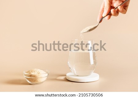 Woman adds psyllium fiber to glass of water on beige background. Superfood for healthy intestines and gluten free diet.