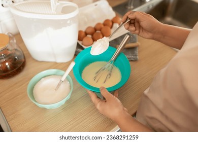 A woman adds sugar with a spoon to the batter for baking pancakes - Powered by Shutterstock