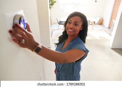 Woman Adjusting Digital Central Heating Thermostat At Home