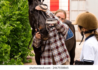 Woman adjusting a horse's bridle in a stable setting. Mentor and student riding school - Powered by Shutterstock