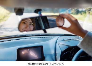 A Woman Adjusting A Rear View Mirror While Driving Car