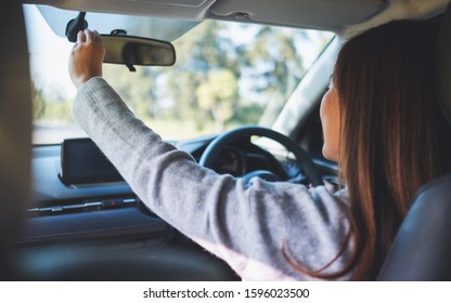 A Woman Adjusting A Rear View Mirror While Driving Car