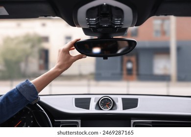 Woman adjusting rear view mirror inside her car, closeup