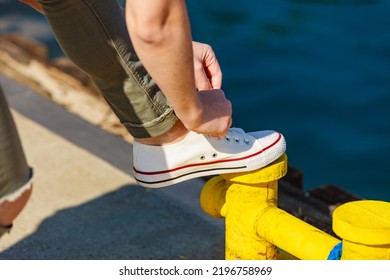 Woman Adjusting, Tying Laces In White Sneakers, Casual Shoes On Yellow Bollard In Marina. Outdoor Footwear.