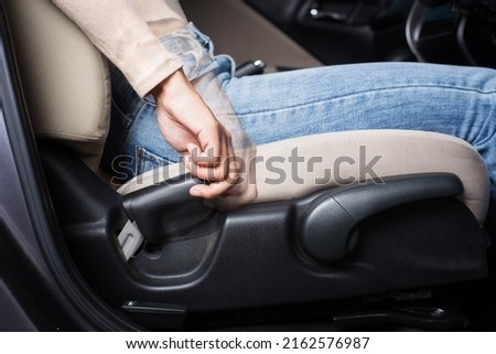 The woman adjusts the driver's seat to the proper position while driving, adjusting the driving position to be comfortable and safe.