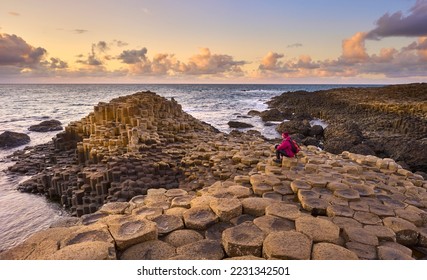 woman admiring sunset between Volcanic hexagonal basalt columns of Giant`s Causeway  in Northern Ireland - Shutterstock ID 2231342501