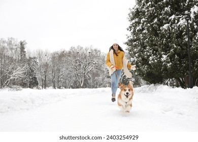 Woman with adorable Pembroke Welsh Corgi dog running in snowy park