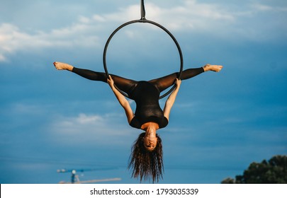 Woman aerialist performs acrobatic element split in hanging aerial hoop against background of blue sky and white clouds. - Powered by Shutterstock