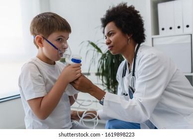 Woman African American Doctor General Practitioner Helping Child To Put Nebulizer Inhaler Face Mask. Asthma Treatment For Children.