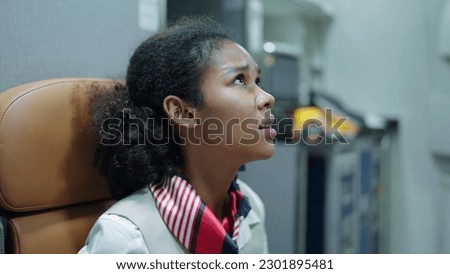 Woman african american stewardess, flight attendant sitting on seat panic and worried on flying through storm turbulence