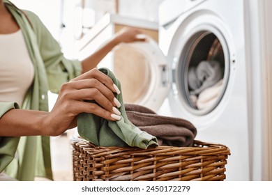 A woman with afro braids cheerfully holds a laundry basket near a washing machine in a vibrant bathroom. - Powered by Shutterstock